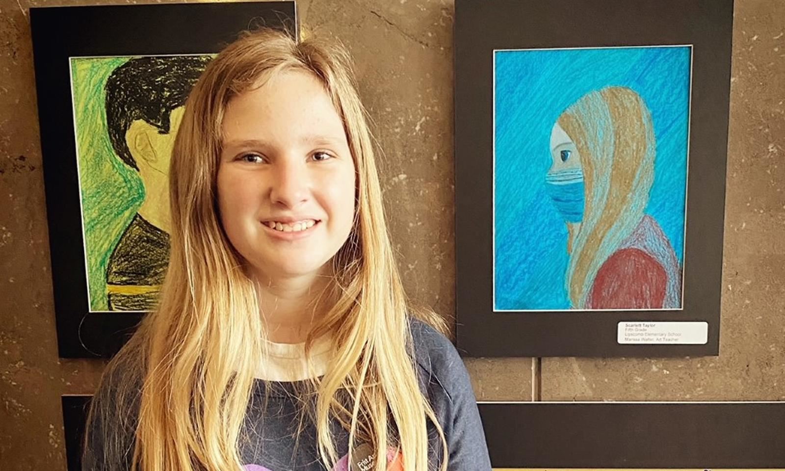A girl smiles next to a piece of artwork